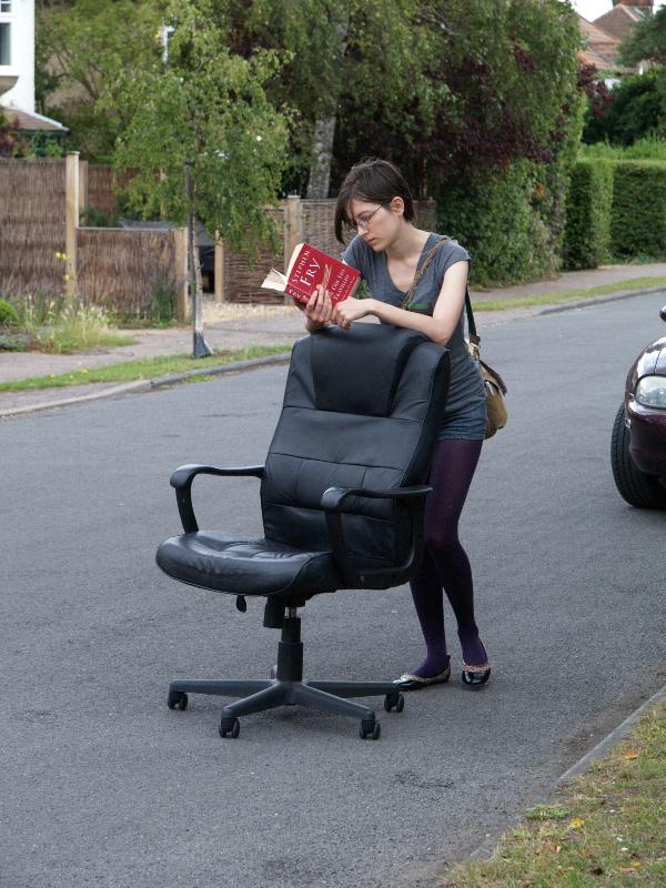 Cambridge, England: Roseford Road: woman walking down the road reading a book and pushing a chair